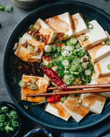 Chopsticks holding a piece of soft tofu with sauce